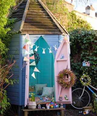 Garden shed painted in mixed pastels, with bunting, spring wreath, and baskets of eggs.
