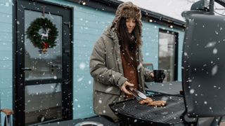 Woman grilling outside in winter, wrapped up warm