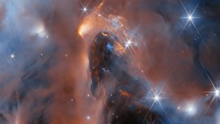 Deep-space photo showing a large orange-brown molecular cloud, with bright stars shining around it