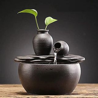 A small ceramic tabletop water fountain. Black pot draining water into a larger ceramic pot.