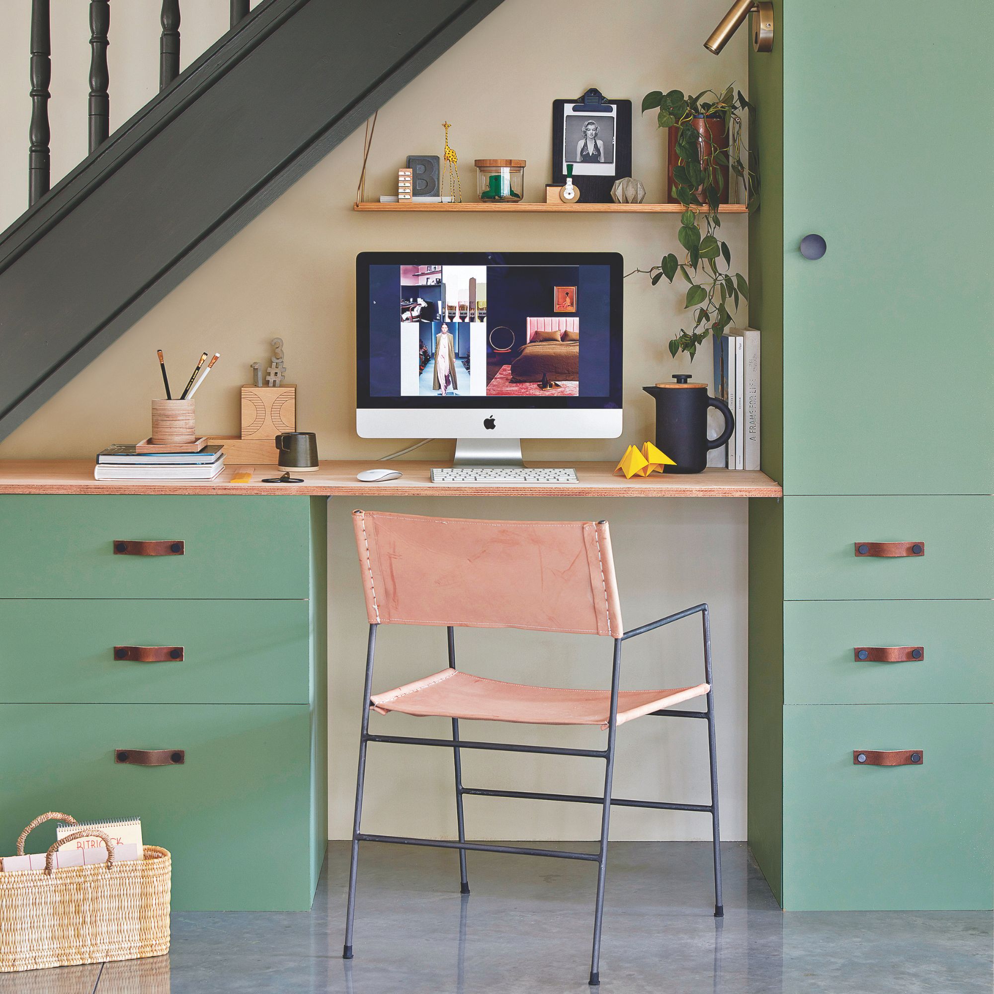Home office setup underneath a staircase, with teal coloured cabinets and a pink chair
