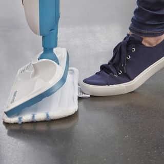 Close up of a foot in a blue plimsole stepping on the mop head of a Black & Decker steam mop.
