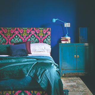 A bedroom painted in royal blue with a vintage blue cabinet and a blue lamp on top of it