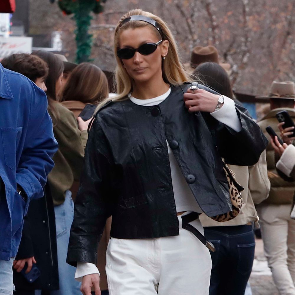 Bella Hadid walks along the pavement outside wearing white jeans with black boots and a black leather jacket.