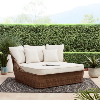a cream and wicker large day bed on a rug in a garden surrounded by hedges