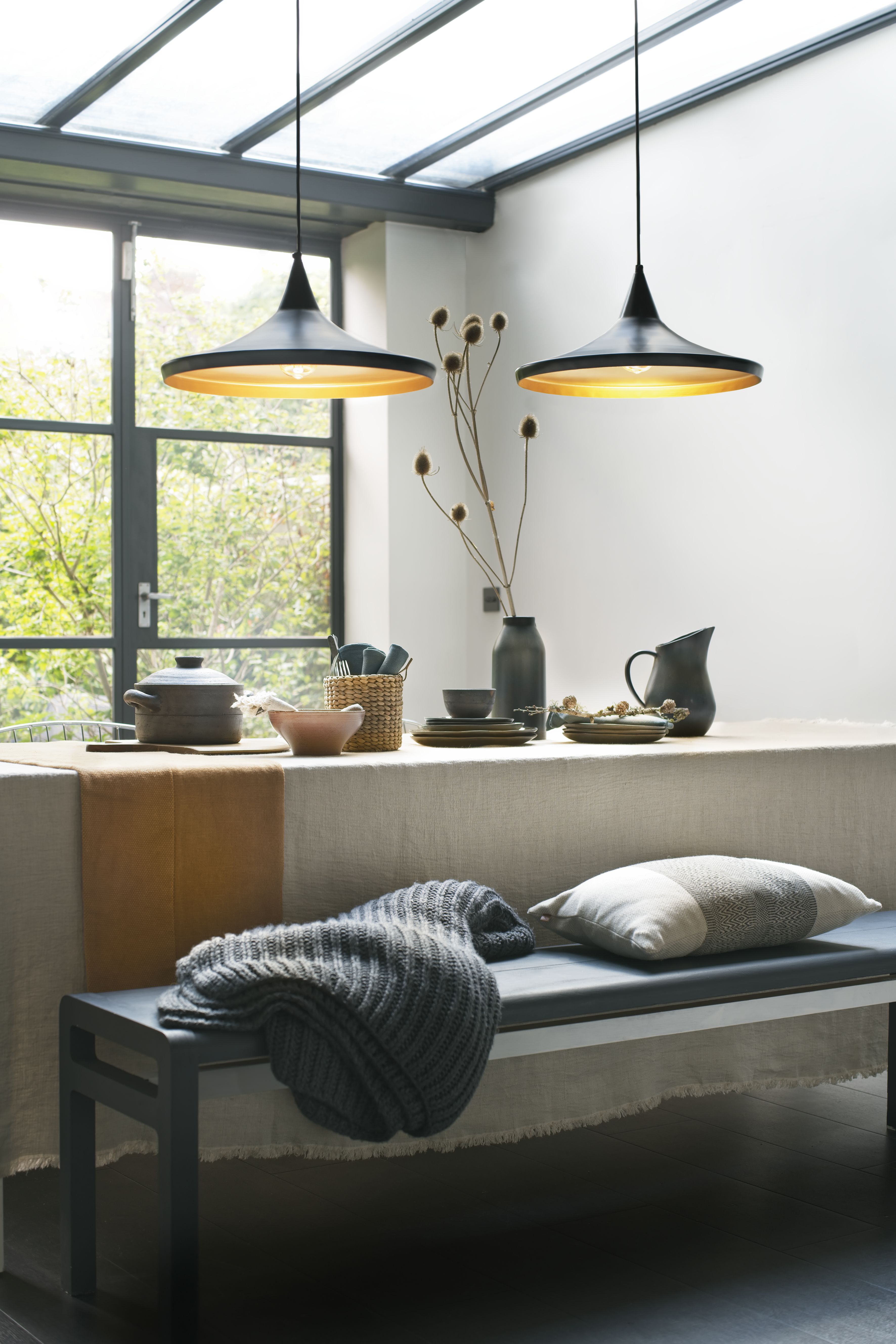 modern rustic dining room with linen tablecloths, knitted throw, bench, linen cushions, black pendant lights and ceramics