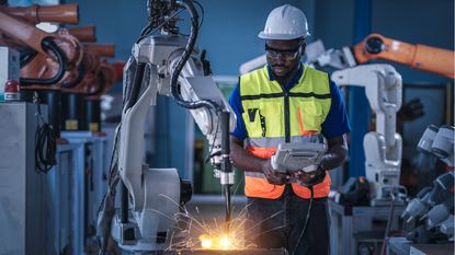An autoworker works with robotics in an auto manufacturing plant.