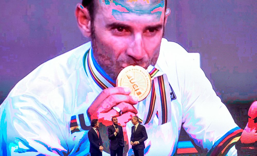 Former pro Pedro Delgado, world champion Alejandro Valverde and Spanish journalist Carlos de Andres stand under a giant portrait of Valverde at the 2019 Vuelta route presentation