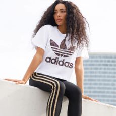 Woman wearing adidas white and brown t-shirt and black leggings sat on concrete