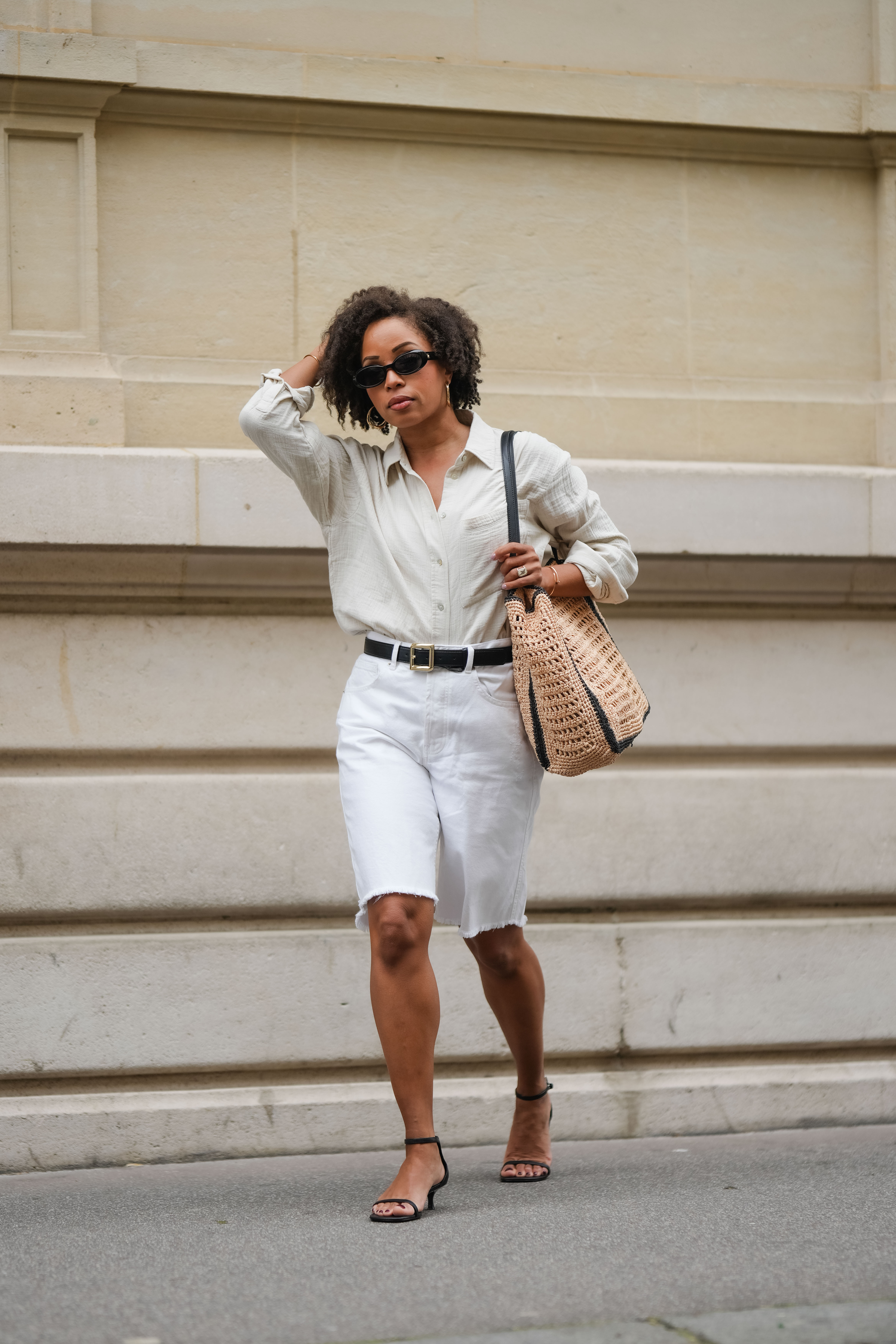 woman wearing button down shirt, white bermuda pants, black heels, and staw tote