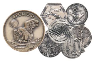 a small apollo 11 medallion showing an eagle landing on the moon, next to six silver medallions showing space shuttle missions