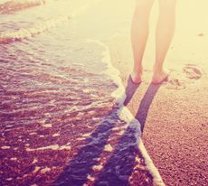 A person walks barefoot on a beach.