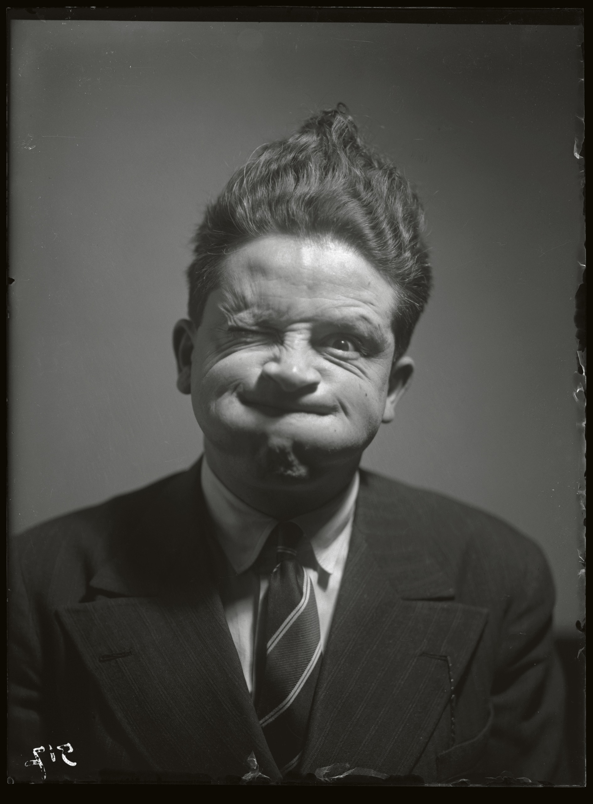 A man in a suit and tie pulls an exaggerated, lopsided grimace for the camera.