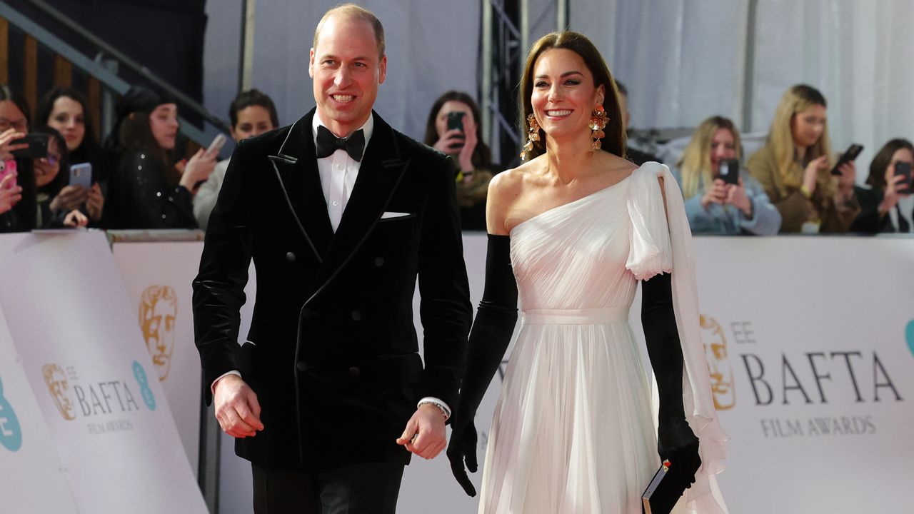 Prince William wearing a tux and Princess Kate wearing a white gown and black gloves walking the BAFTAs 2023 red carpet