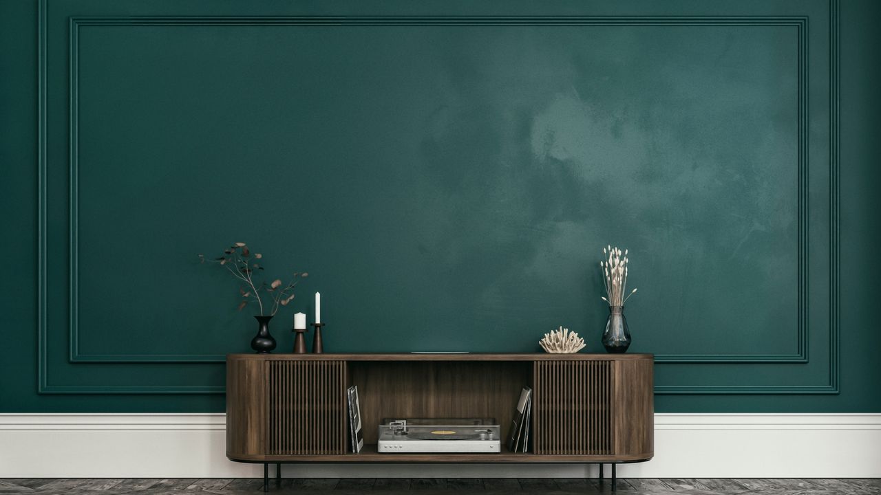 Landscape wide shot of a dark green living room wall with paneling and a rounded sideboard with dark wooden floor