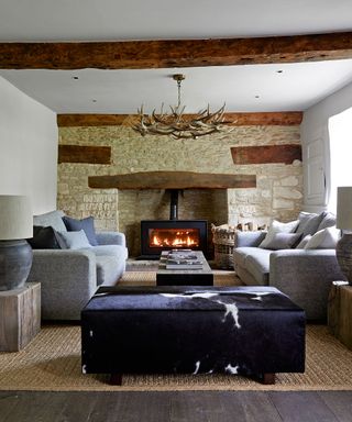 Living room with fireplace and exposed stone wall, gray sofa, antler chandelier and cowhide stool