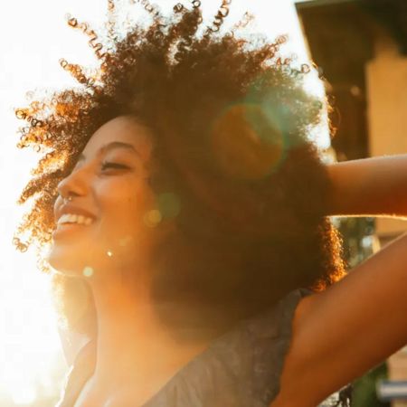 Woman with afro smiling in the sunshine - best akro fragrances