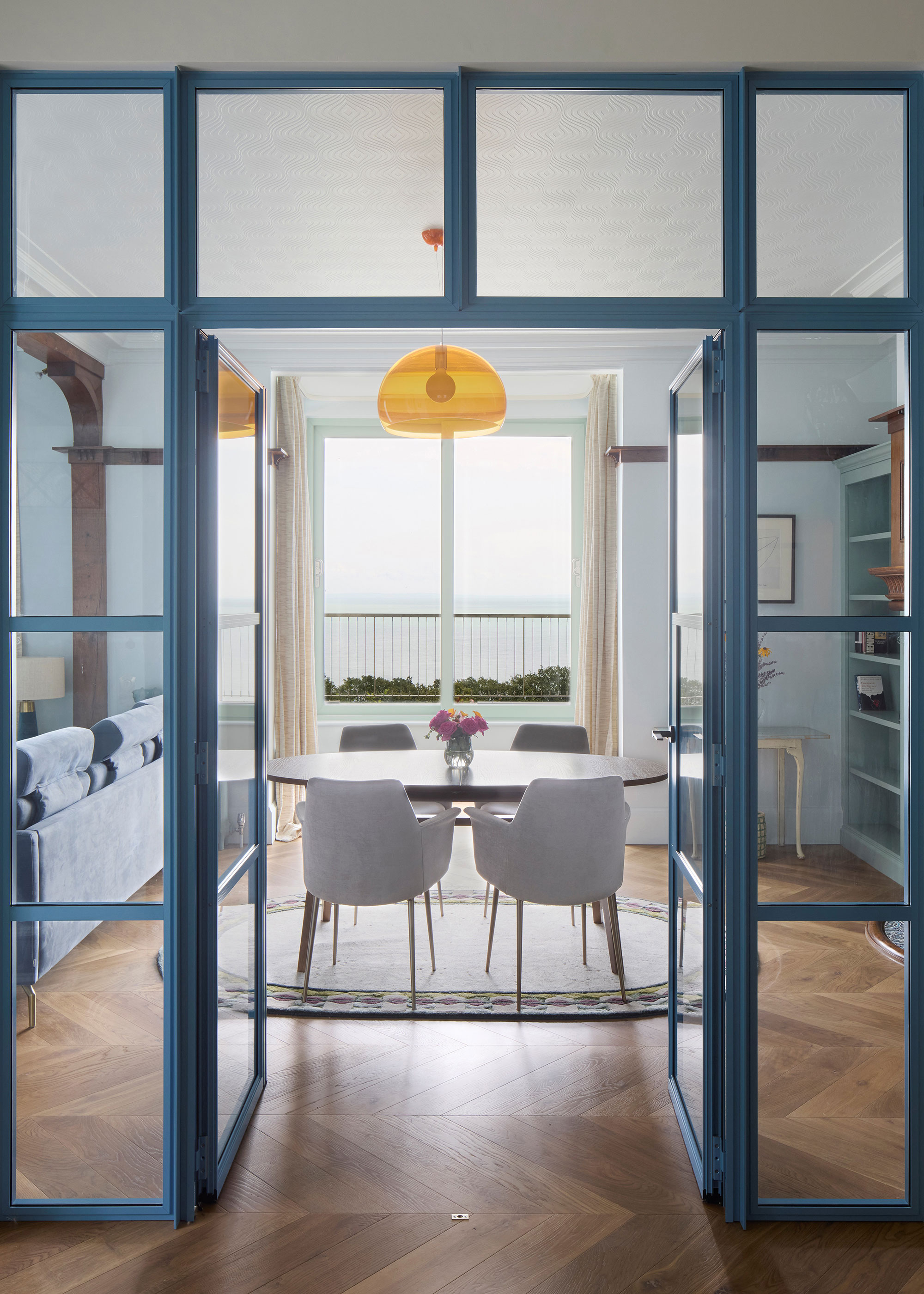 blue framed glass doors leading to open plan dining living room with herringbone wooden flooring