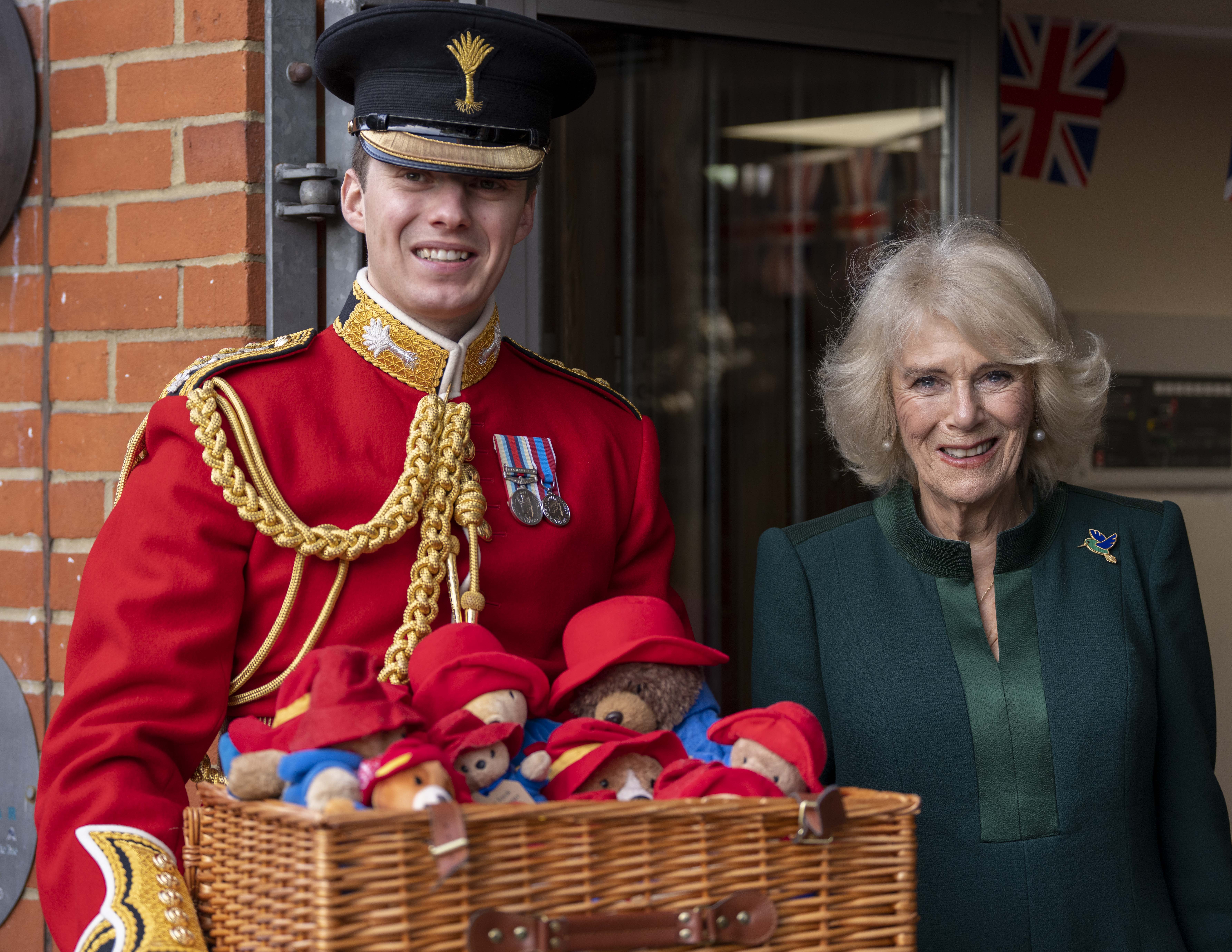 Queen Camilla standing with a soldier carrying a basket of Paddington bears