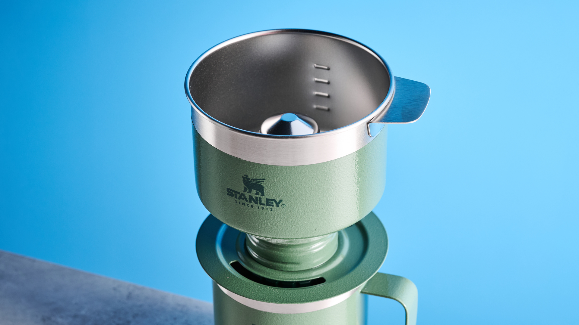 the stanley perfect brew pour over coffee maker in green, photographed with its companion travel mug and with the metal built in filter
