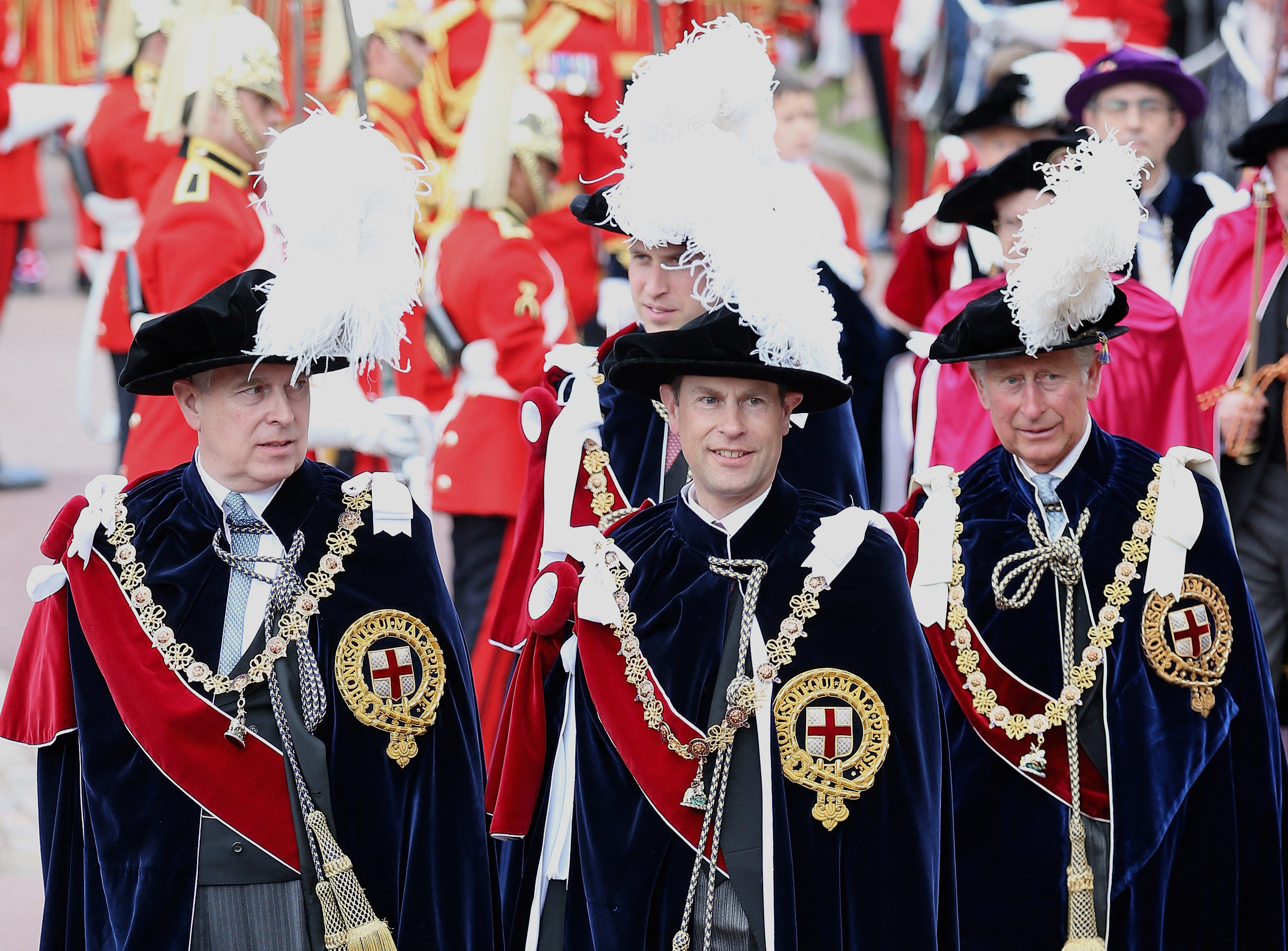 Prince Andrew attending Garter Day wearing long ceremonial robes and a black hat with a large white feather protruding from the top and a red sash and a gold chain
