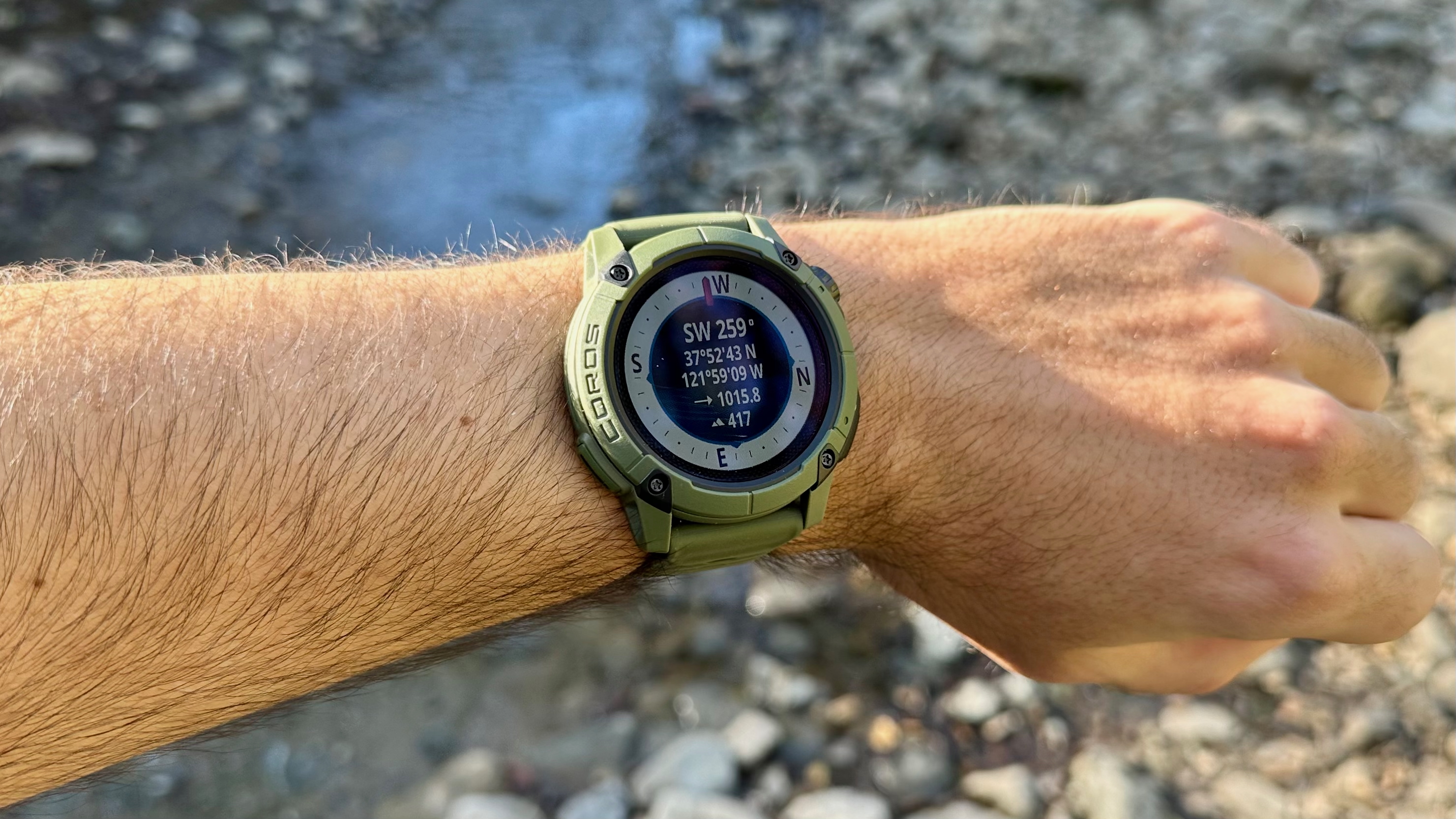 Photo of the COROS NOMAD with the compass open, with a rocky stream visible behind it.