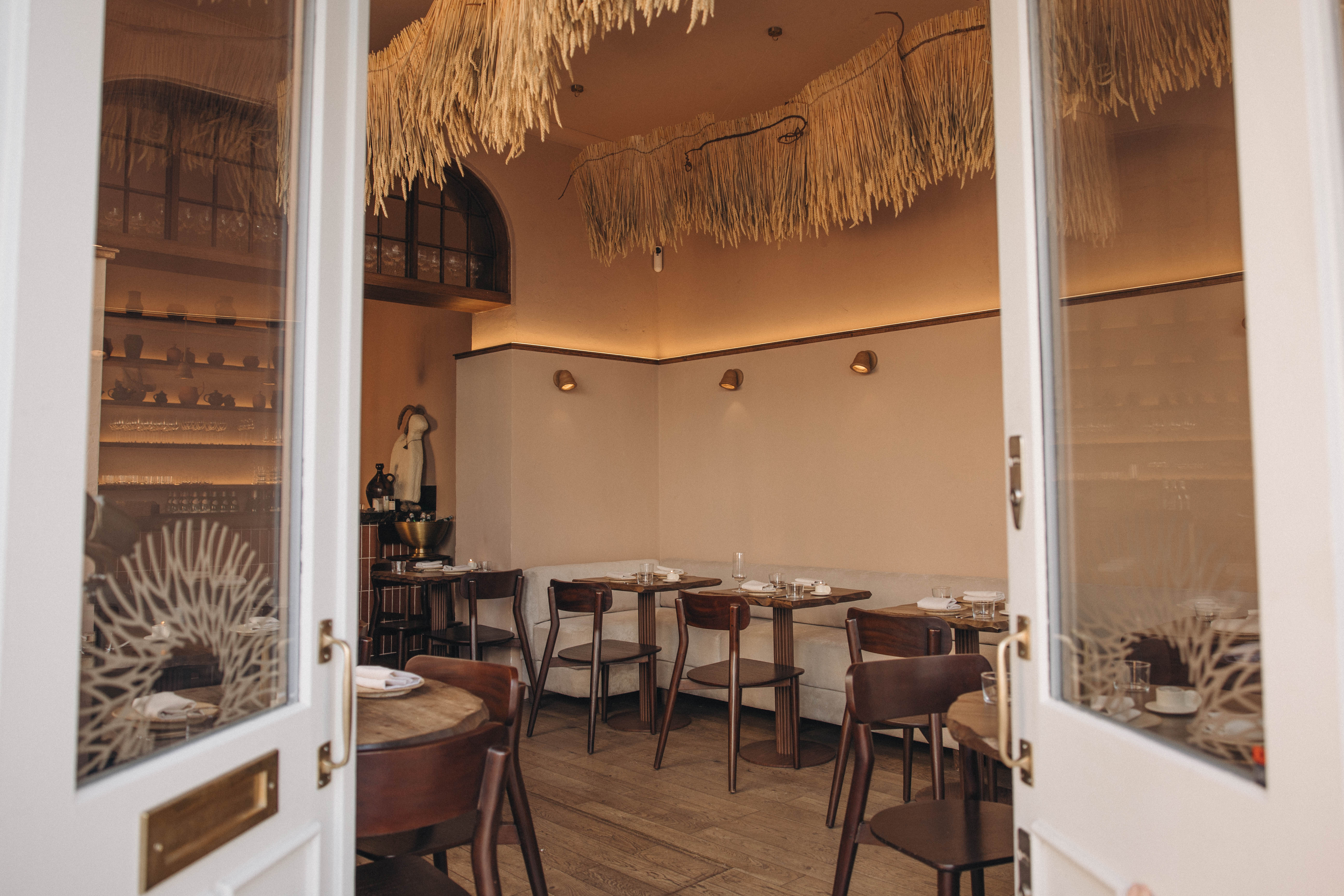 A crafty restaurant interior furnished with cream and brown pieces, a rattan-made, pendant sculptural installation, and back-lit, warm surfaces.