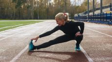 Woman stretching lower body on running track, wearing athleisure