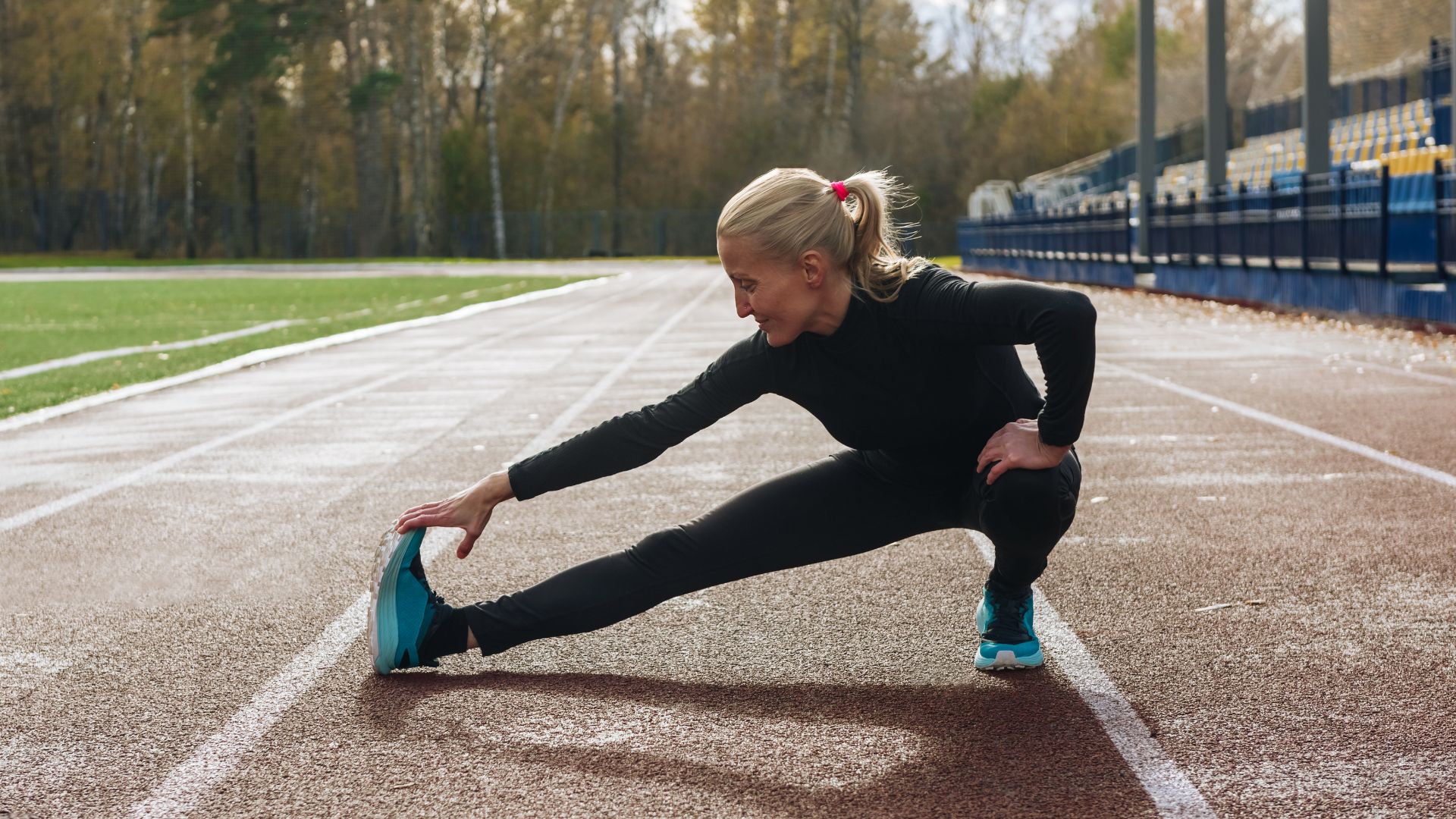Woman stretching lower body on running track, wearing athleisure