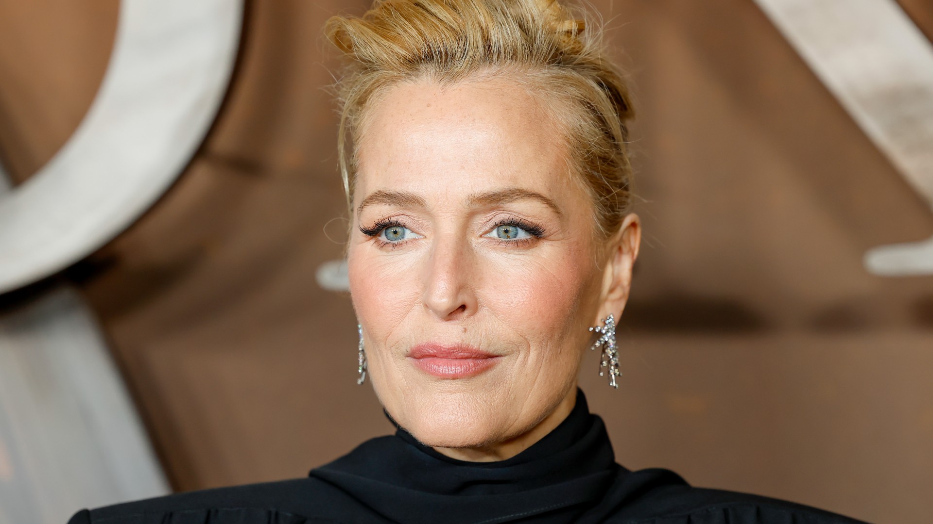 a close up paparazzi photo of a woman posing on a red carpet in front of a brown backdrop