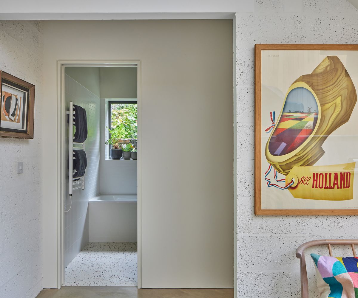 A view looking into a small downstairs bathroom with terrazzo floor tiles. In the foreground there is a bright framed poster on a white wall