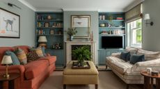 A blue sitting room with an orange sofa, yellow ottoman and bookshelves
