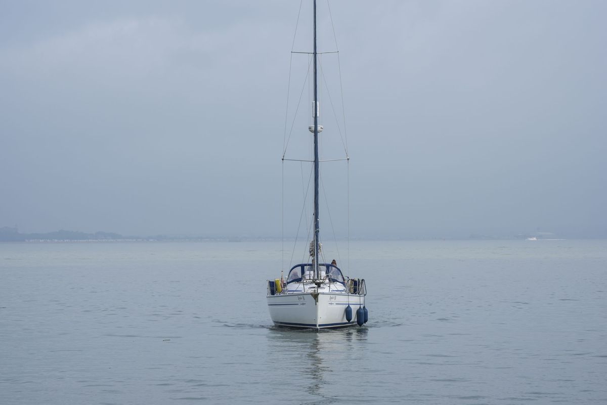 A sail boat, sail packed away, motoring straight ahead on a calm ocean