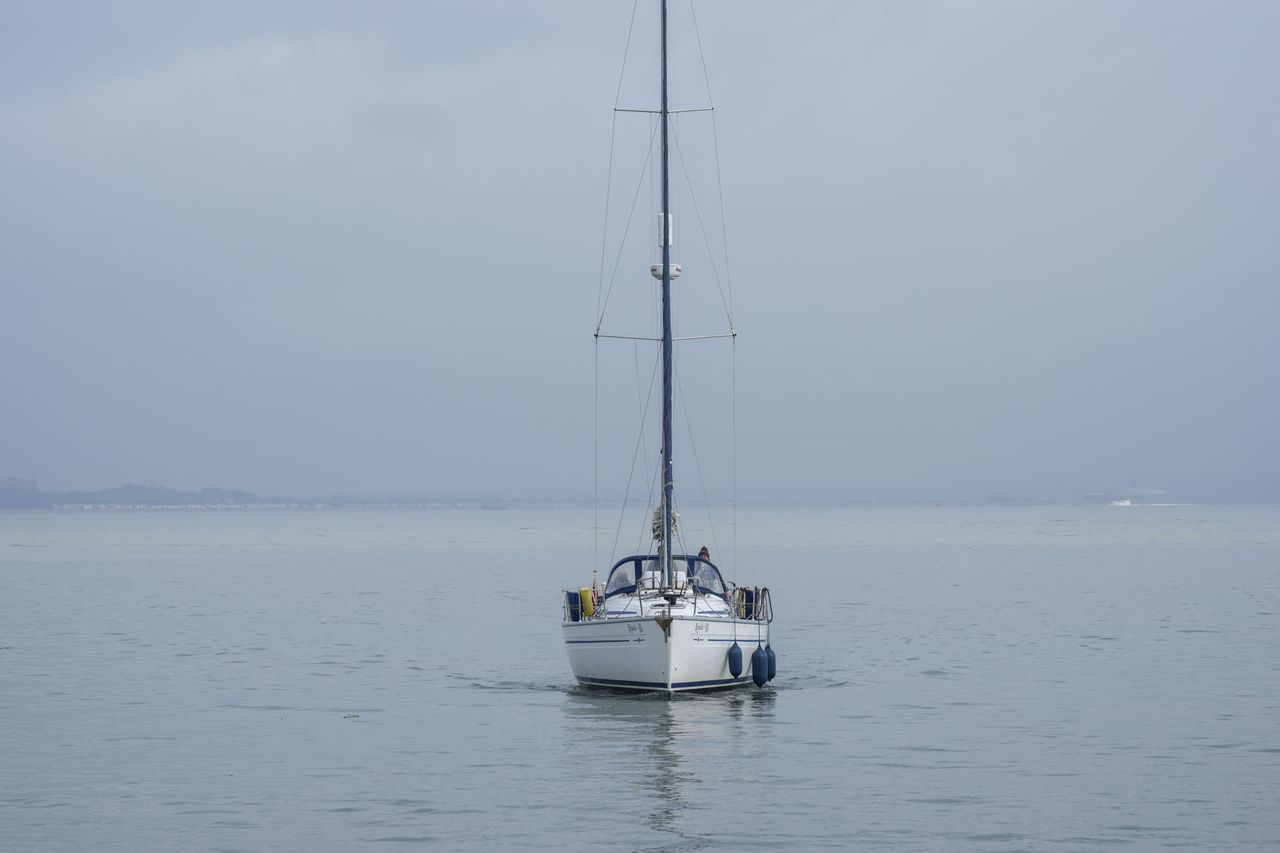 A sail boat, sail packed away, motoring straight ahead on a calm ocean
