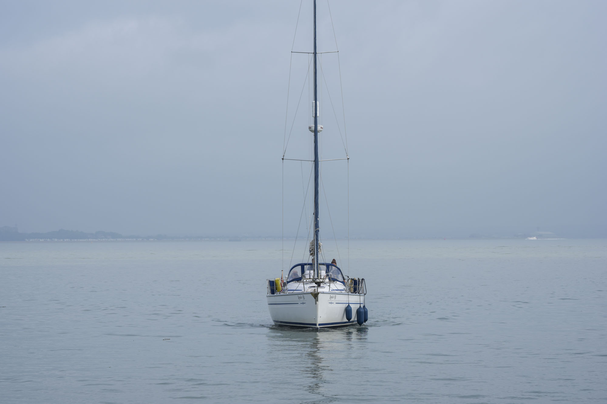 A sail boat, sail packed away, motoring straight ahead on a calm ocean