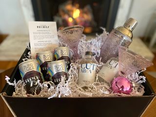 A gift box with Godinger pink crystal martini glasses and a crystal cocktail shaker and Blind Tiger French 75 mocktails and Cut Above Zero Proof tequila and gin bottles