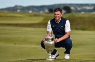 A golfer poses next to the Amateur Championship trophy