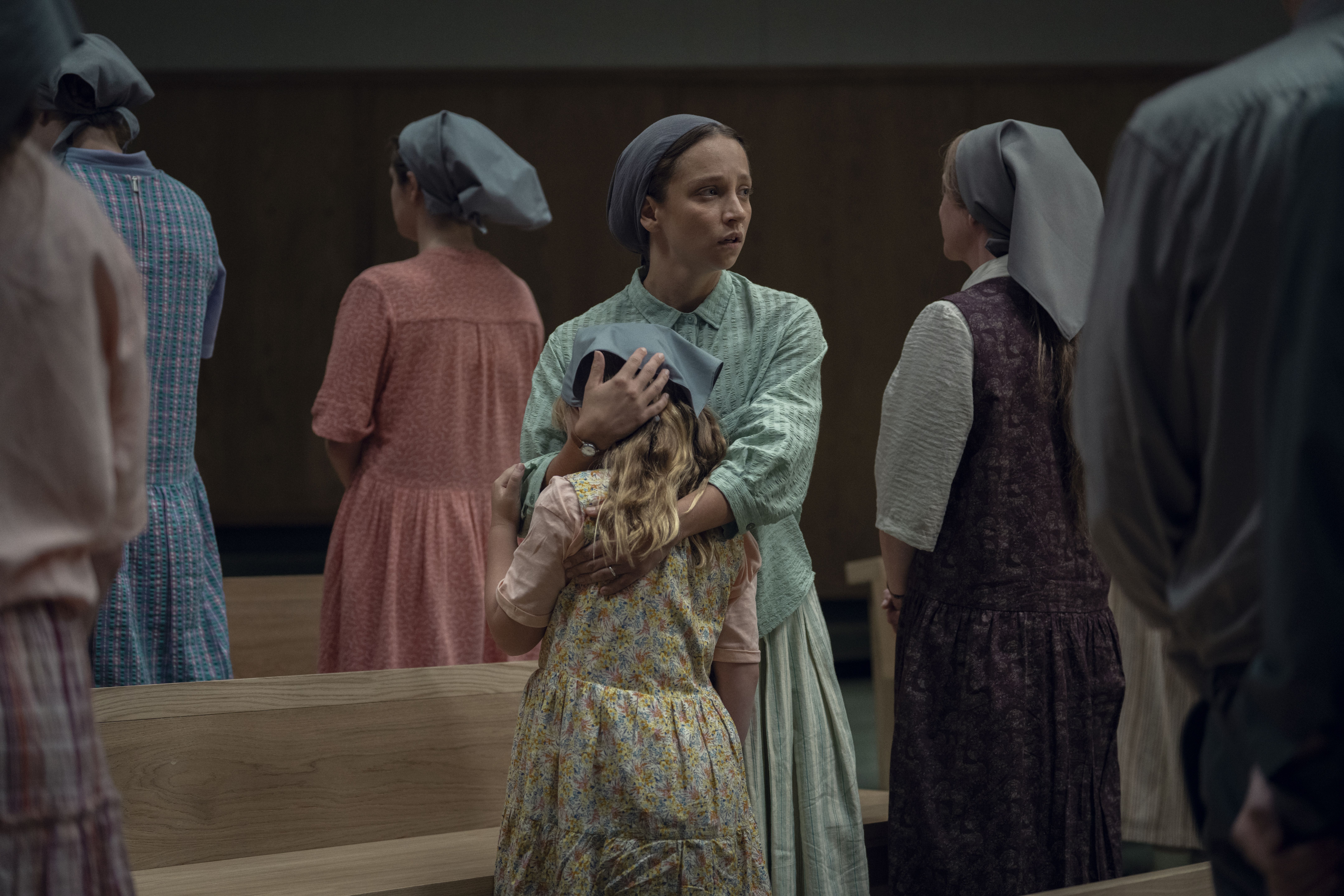a woman in traditionalist clothes covers her daughters face while standing in church pews in a still from netflix's unchosen