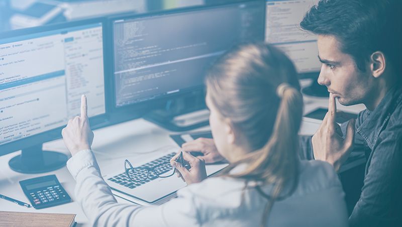 Two developers working on a project in front of a computer screen