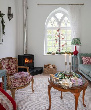 living room with arched gothic style window, pale walls and log burner with traditional furniture