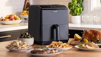 One of our picks for best air fryer, the Cosori Dual Blaze, on a countertop with cooked chicken, fries, salad and vegetables