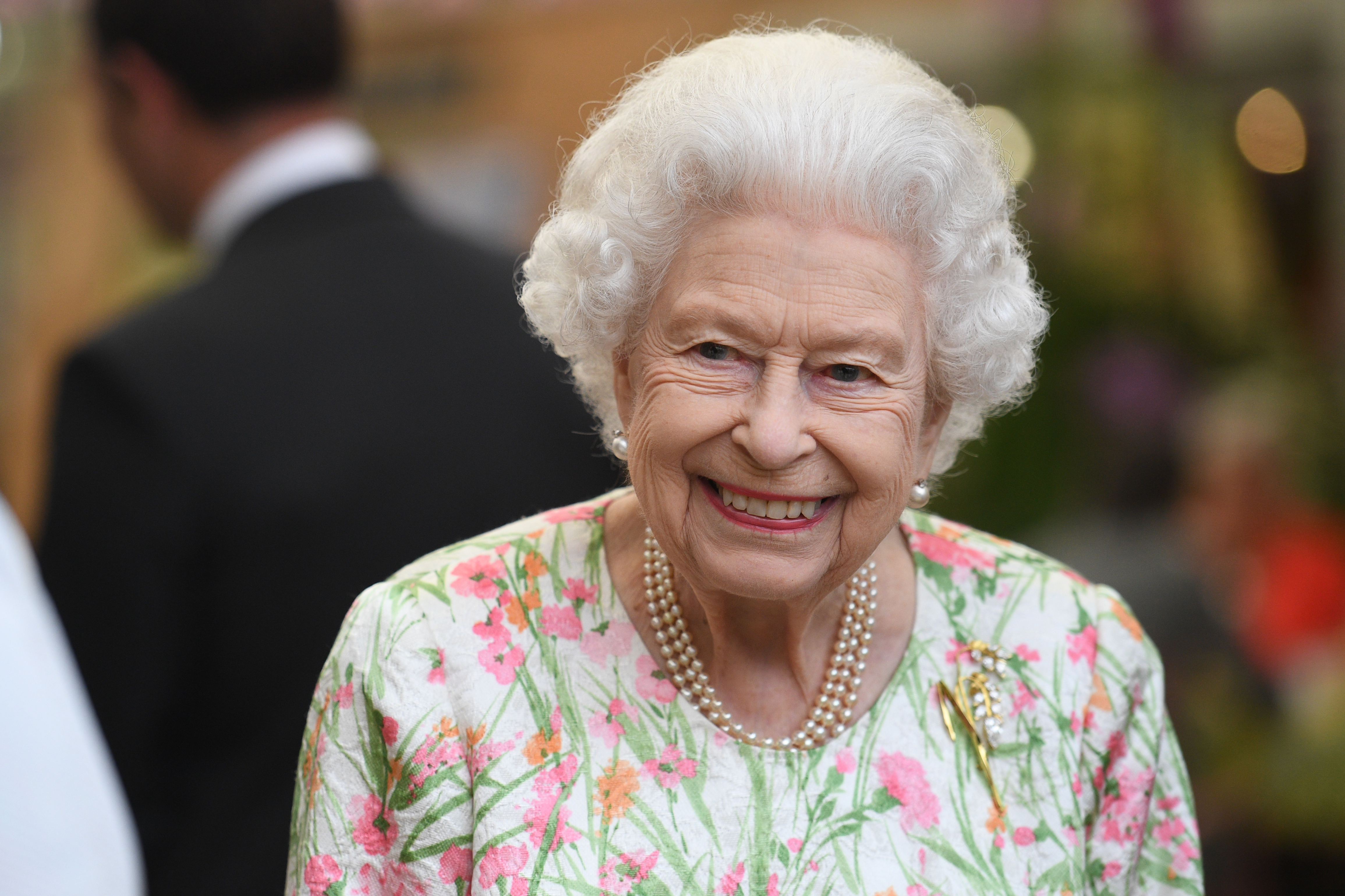 Queen Elizabeth wearing a white dress with flowers and a string of pearls and smiling