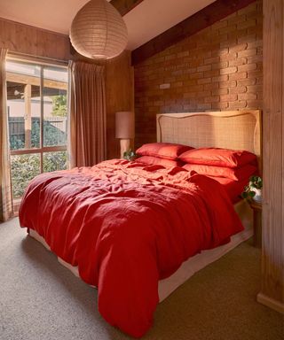 Paprika sheets on a wooden headboard against exposed brick walls.