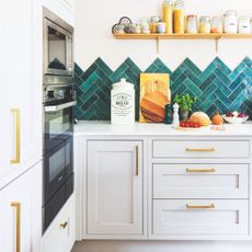 White painted kitchen with teal chevron tiles, a white worktop and grey kitchen cabinets with gold handles