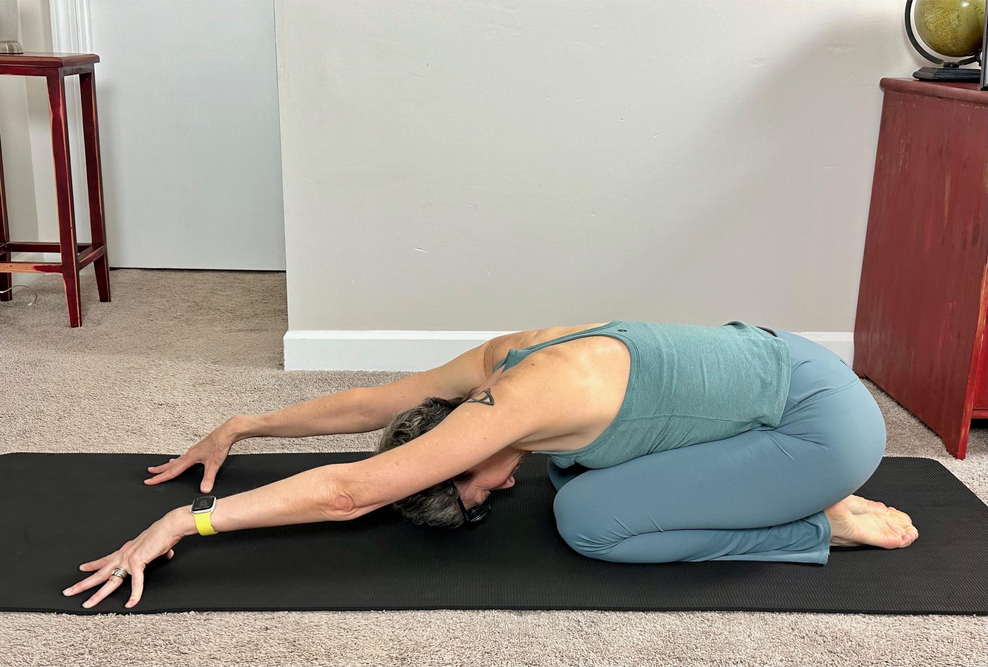 woman performing child's pose on a black yoga mat on carpet floor
