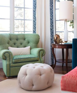 A living room with a pistachio green chair, a white upholstered ottoman with storage space and a large window behind the seats