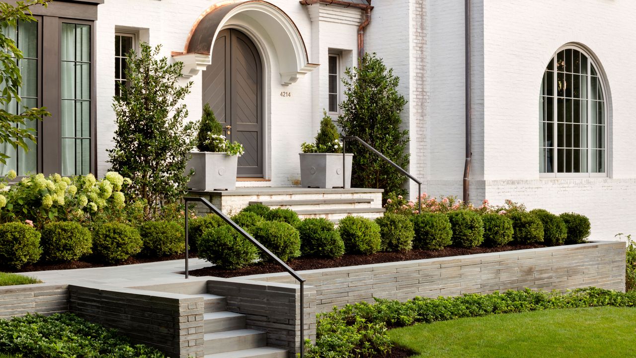 landscaped approach to arched front door with clipped box balls and grey slate walls and steps white rendered house