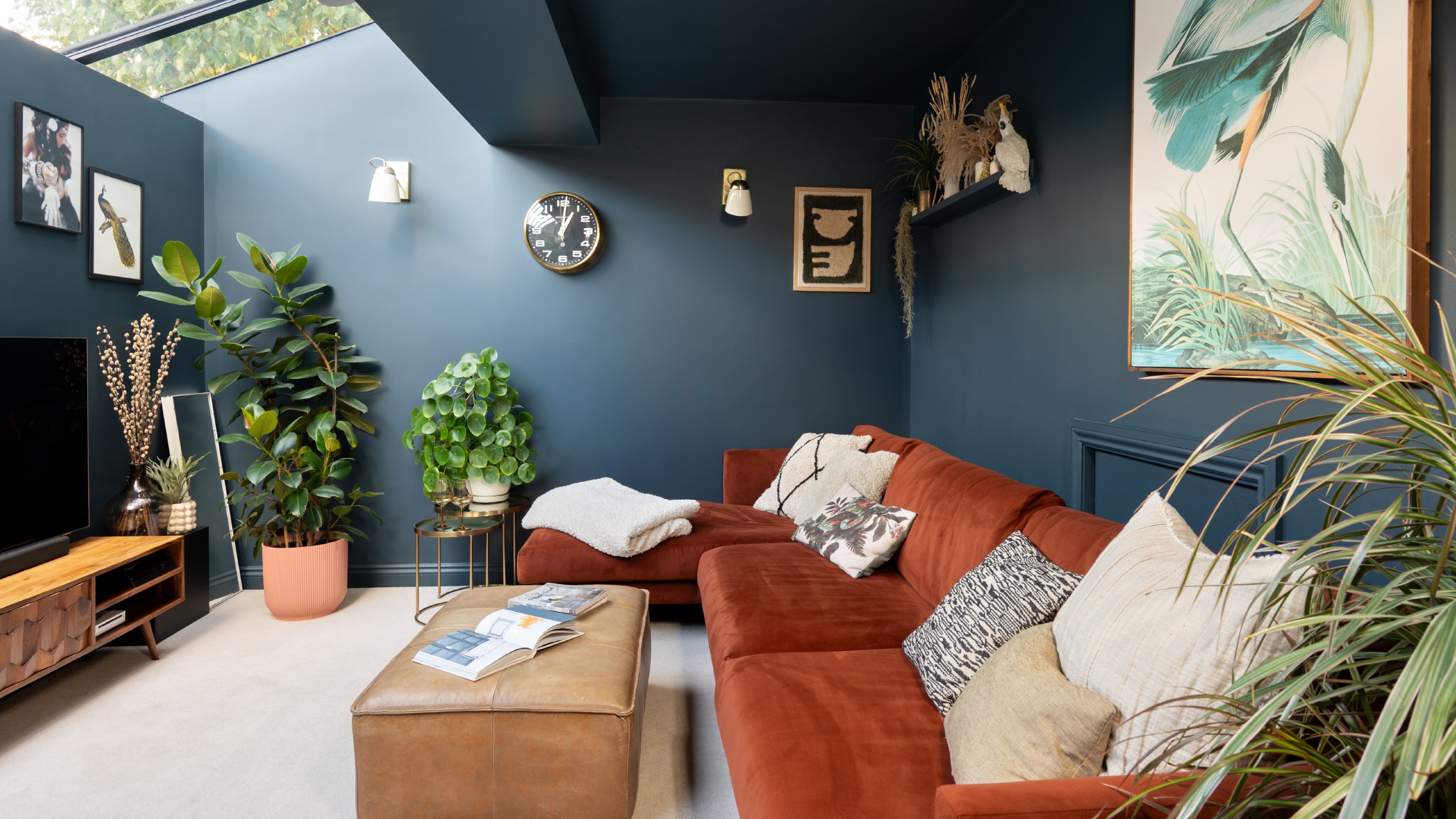 A living room with a skylight colour drenched in dark navy blue paint with a rust-coloured chaise sofa