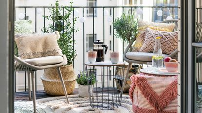 Spring-summer styled balcony in urban setting, with tufted pouffe, natural textures, and casual lounging set-up with coffee