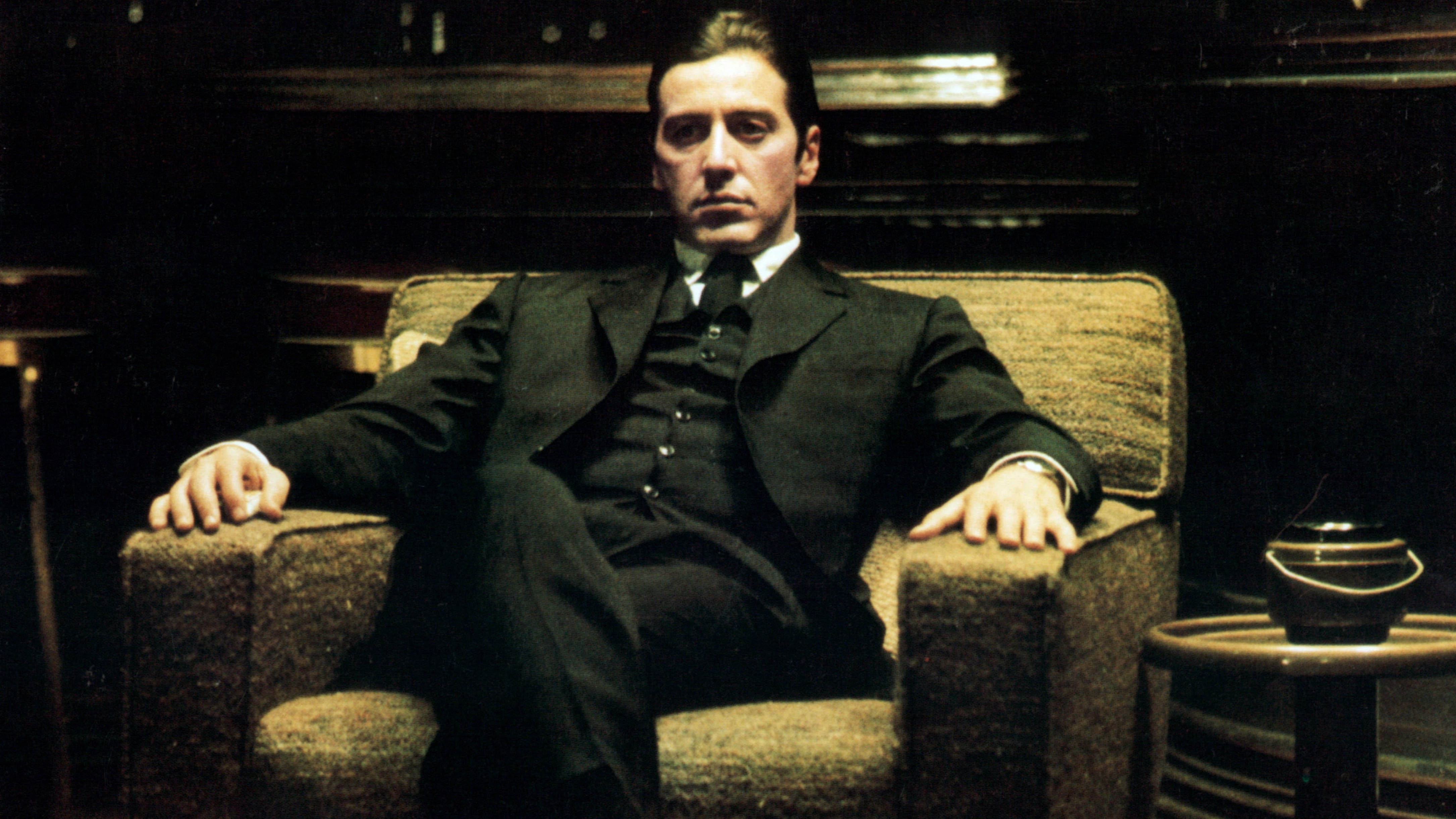 Al Pacino sitting down on a chair with a stern look on his face.